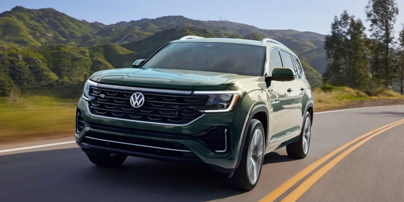 Green Volkswagen Atlas SUV driving on a scenic mountain road.