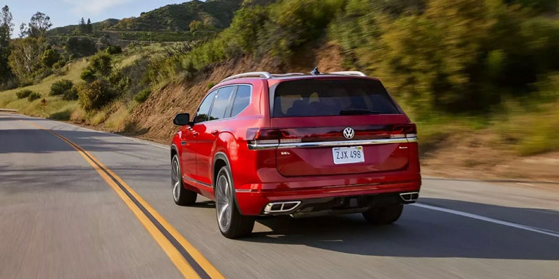 Red Volkswagen Atlas driving on a highway with a mountain backdrop.